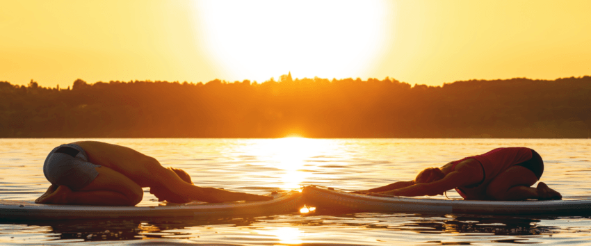 two people doing yoga on a lake with a beautiful sunset