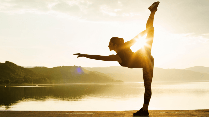 a girl is doing yoga beside the lake